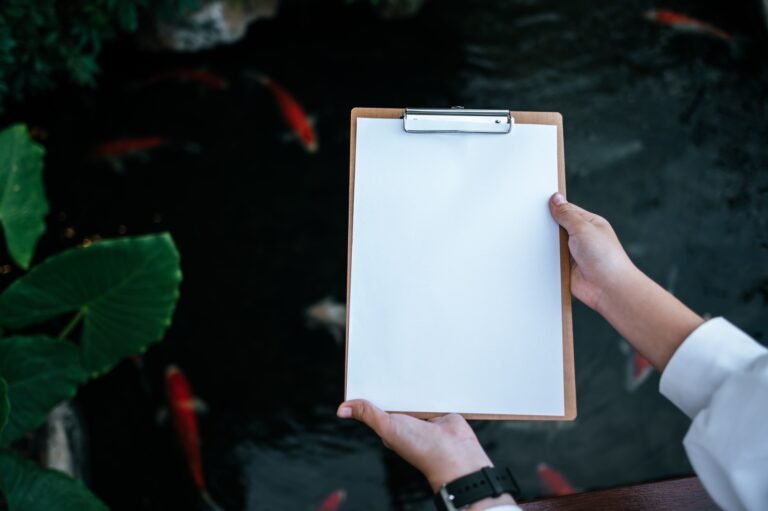 A hand holding a clipboard on a fish pond