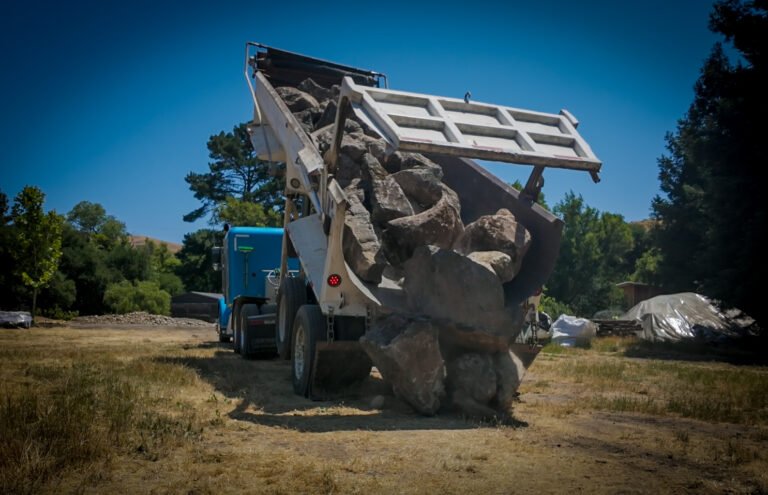 Dump truck unloading rocks on dry field